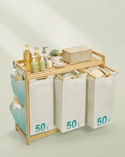Tokari bamboe wasmand met drie witte 50L waszakken en zijvakken voor extra opbergruimte in een lichte kamer.